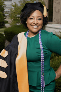 Black woman in a green dress poses with doctoral cap and gown