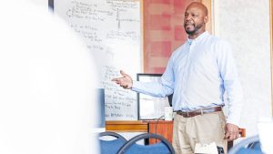 Black, male business professor stands in front of a class teaching