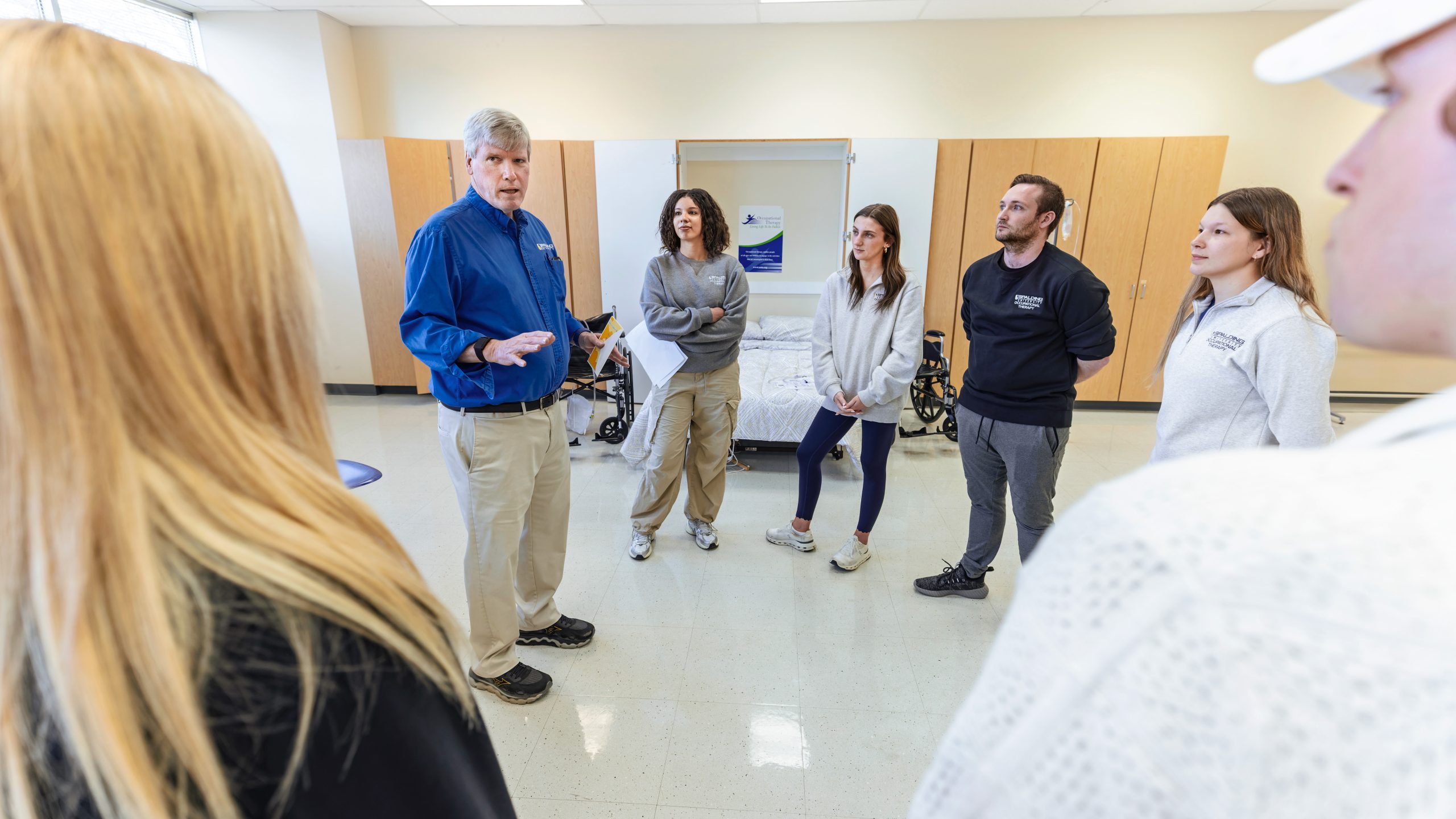 Group of occupational therapy students stand in a lab talking to professor