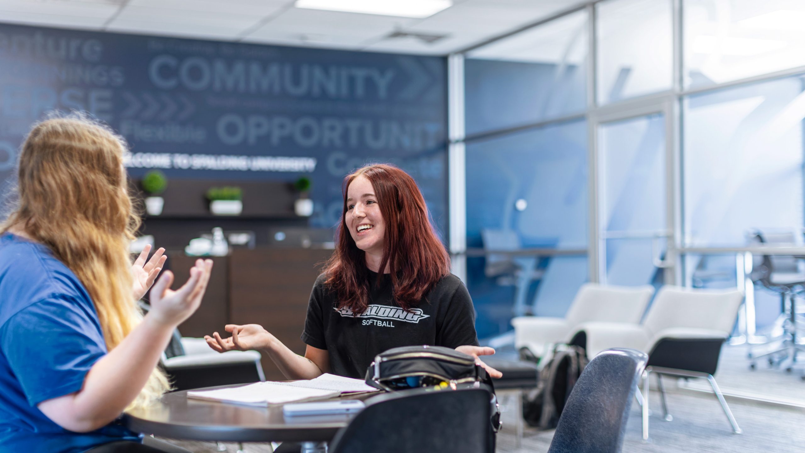 two female students sitting at a table talking and smiling