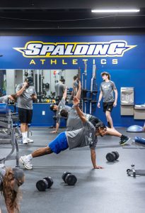 Spalding student athletes in plank position in weight room with other students in background