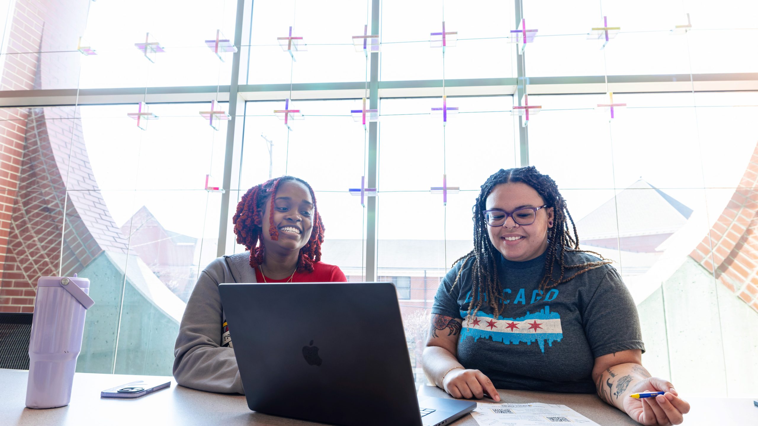 Two black female students visit in front of a laptop computer