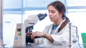 female student in lab coat looking into microscope