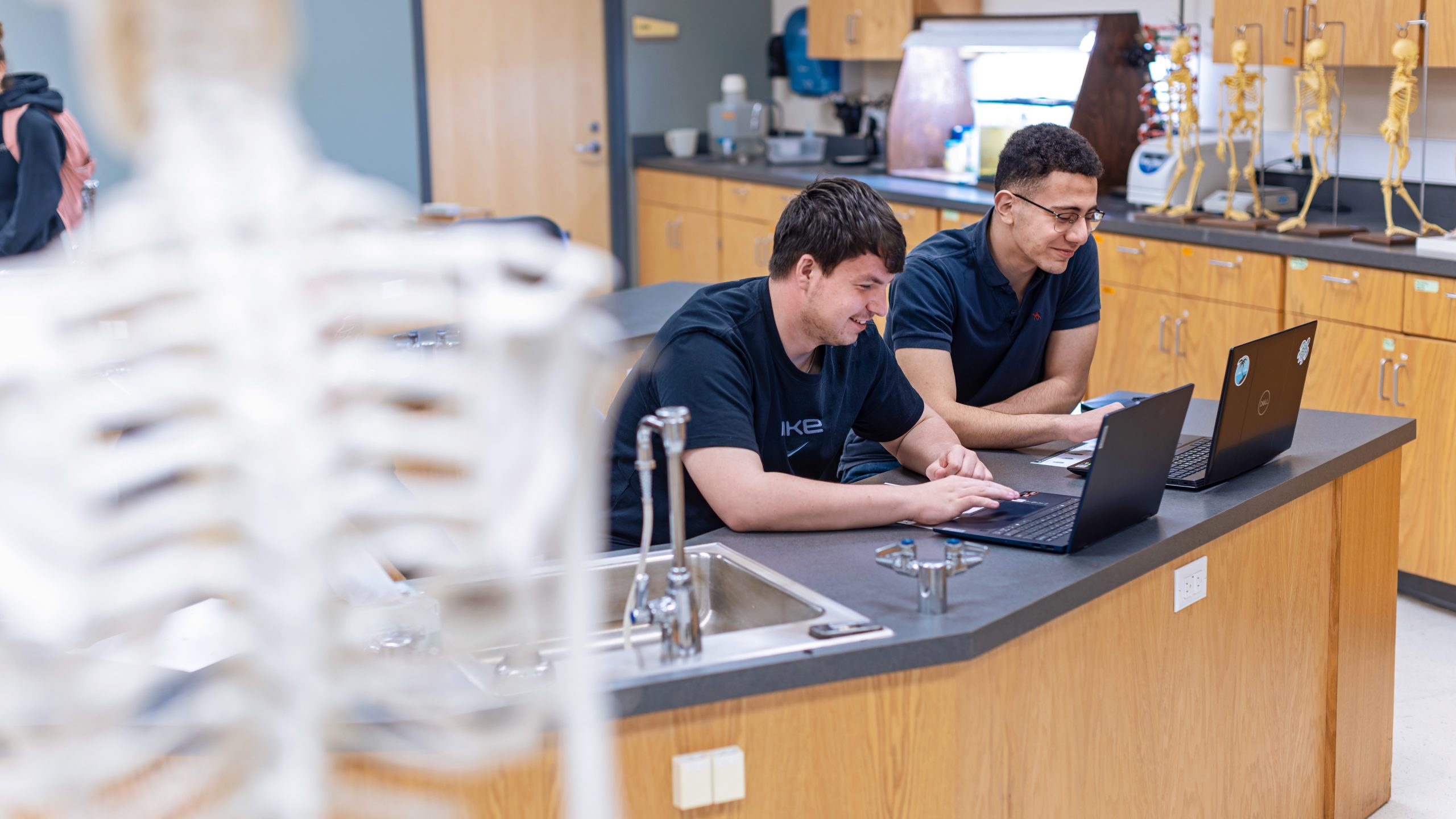 Two male students work at laptops in a biology lab