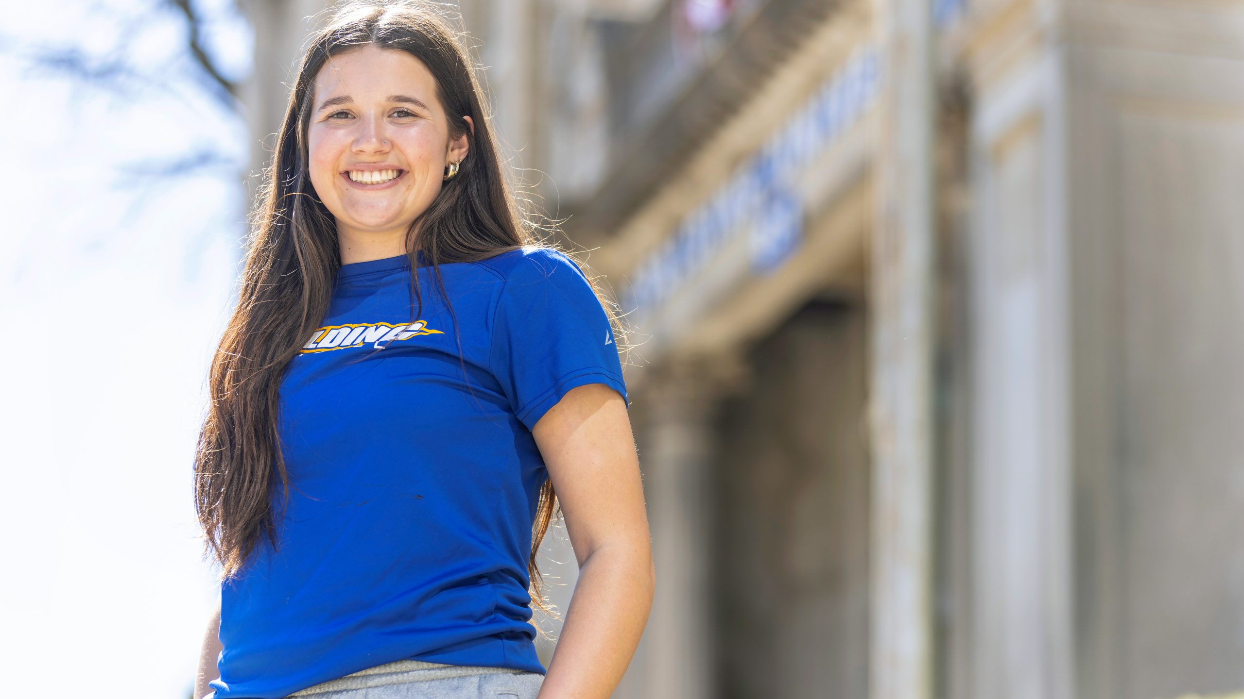 Female student with long brunette hair smiles wearing a blue Spalding t-shirt