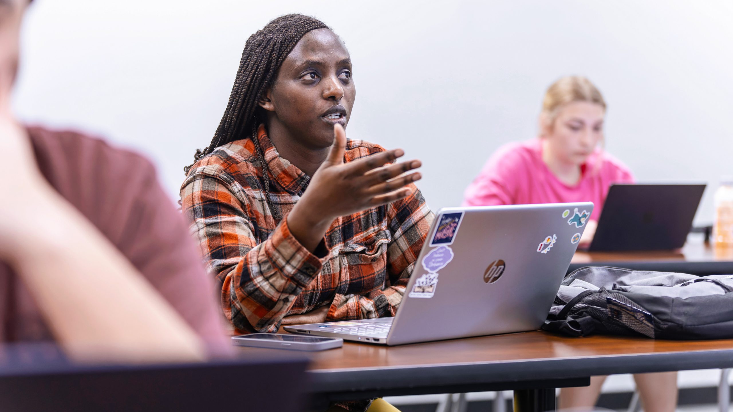 female student speaking in class with laptop open on desk in front