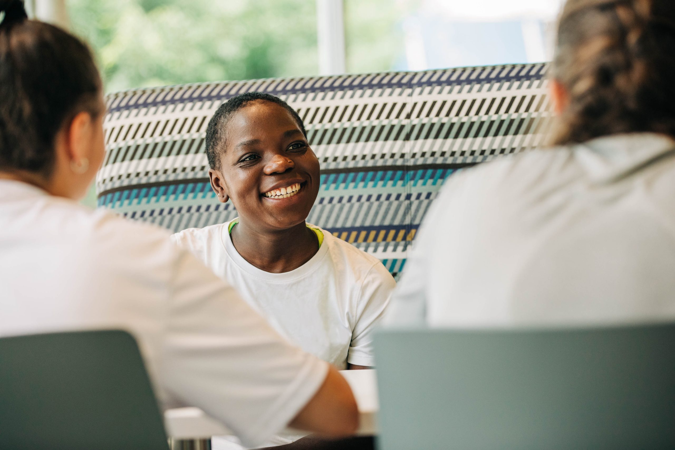 Black female student smiles at two other female students sitting across a table
