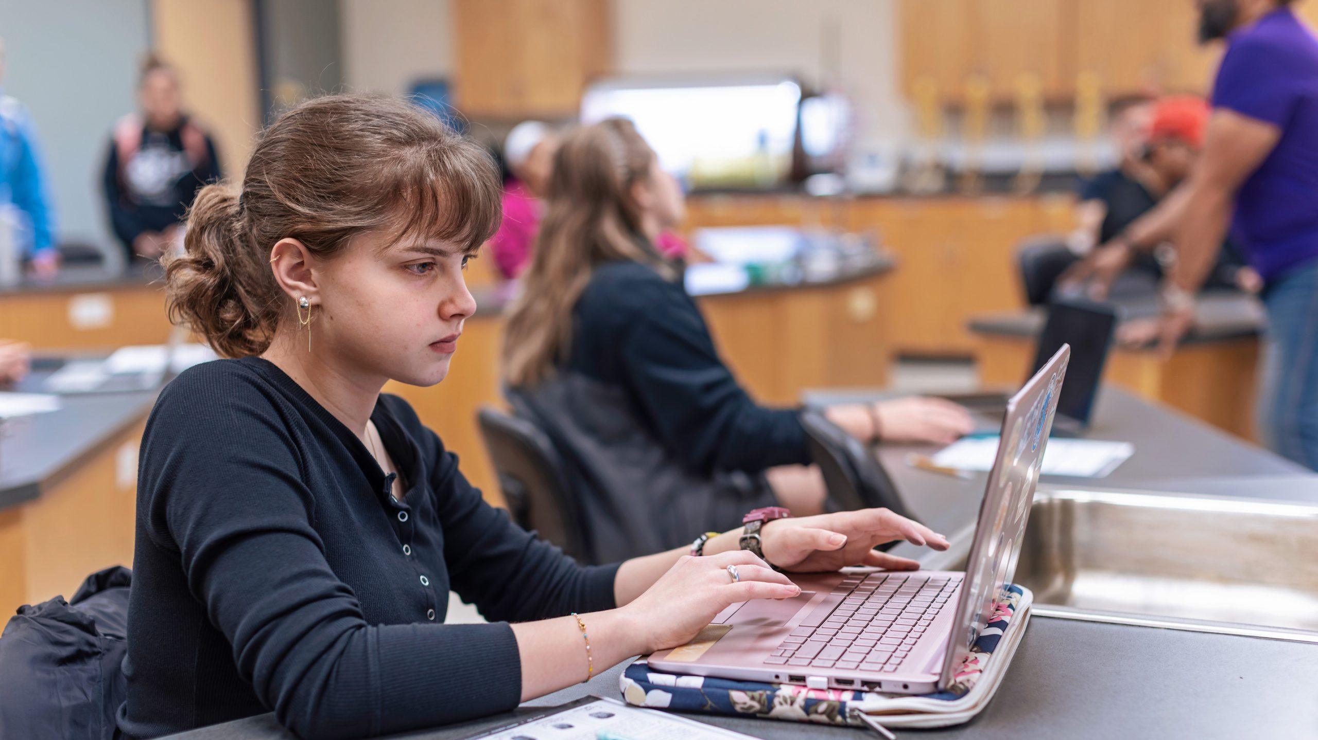 A small group of students work on laptops in a science lab setting
