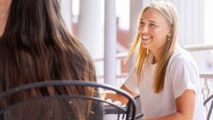female student with blond hair sits at a table outdoors with another student