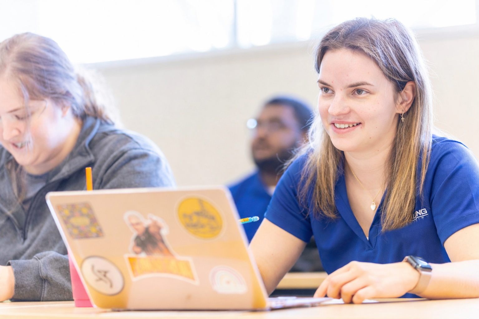Female student with a blue Spalding polo shirt sits with her laptop in a bright classroom setting