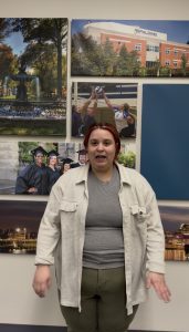 Female student in doctor of social work program talks directly to camera in front of a wall with photos