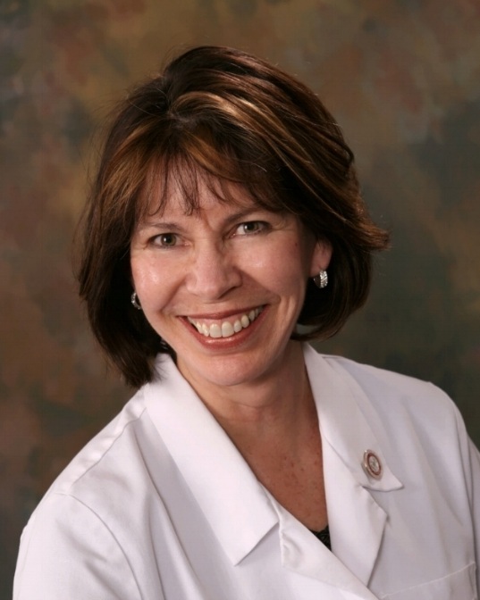 Middle aged woman wearing white shirt with short brown hair smiles directly at camera